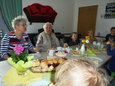 Senioren und Kinder sitzen gemeinsam im Veranstaltungsraum im Mehrgenerationenhaus sOfA am Tisch und genießen das Osterfrühstück.