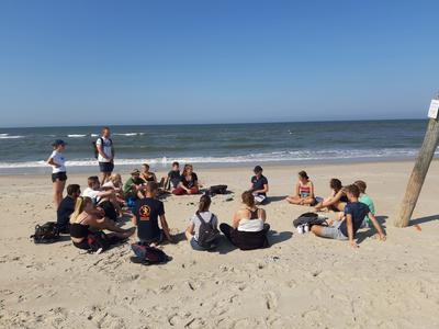Eine Gruppe Jugendlicher sitzt bei blauem HImmel im Sand am Strand von Norderney.